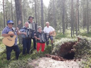 hedlunds 5 personer med gitarr, dragspel och ukulele som står bland blåbärsris i en tallskog